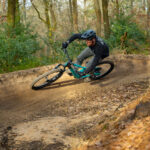 A rider on a Scott Full-Suspension mountain bike rides around a bermed corner