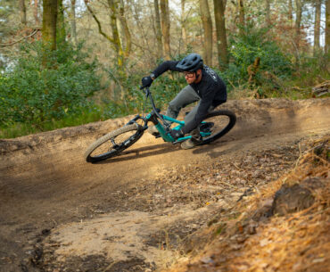 A rider on a Scott Full-Suspension mountain bike rides around a bermed corner