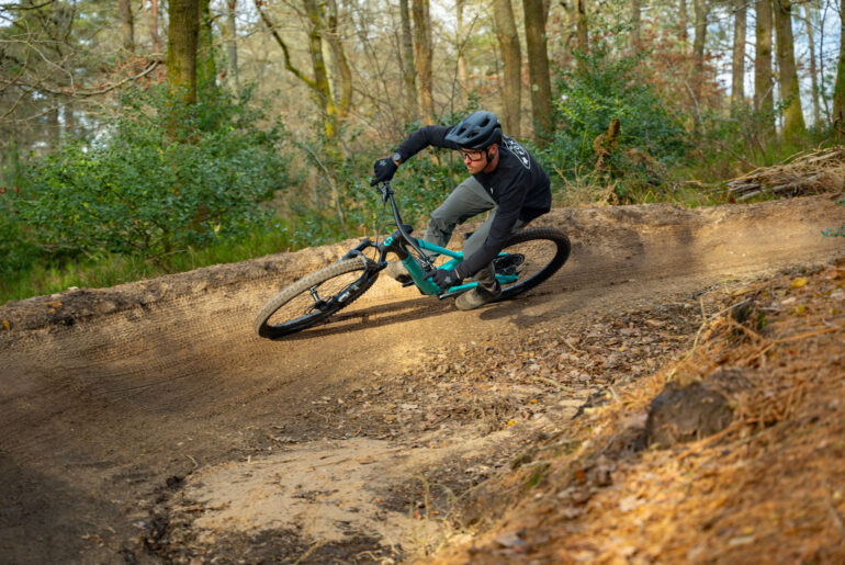 A rider on a Scott Full-Suspension mountain bike rides around a bermed corner