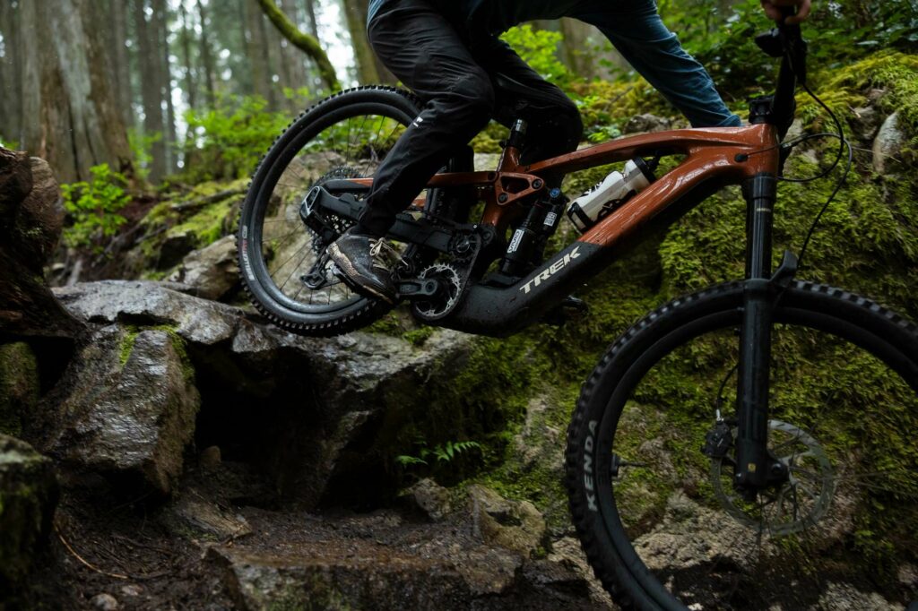 A Trek Slash+ electric mountain bike being ridden over some mossy rocks