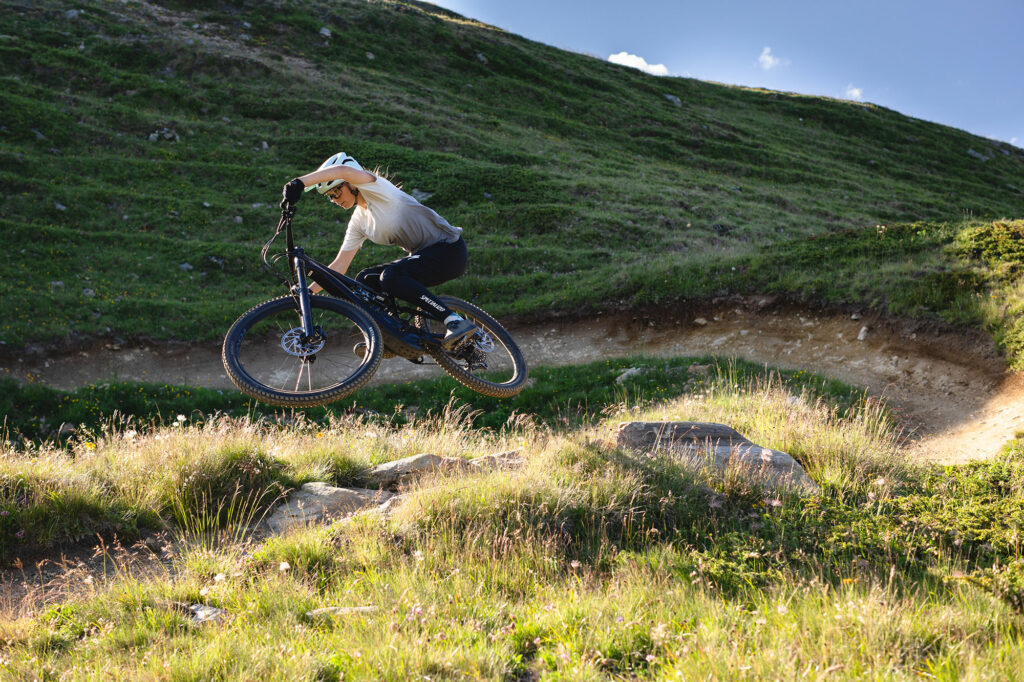 A female mountain biker jumping out of a banked corner on a specialized turbo levo sl