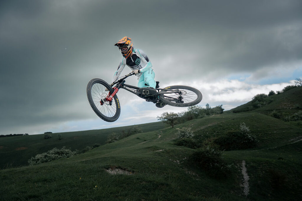 A downhill mountain bike rider in the air over a jump wearing a troy lee designs D4 carbon full face mtb helmet